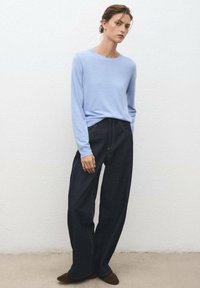 Light blue long-sleeve sweater paired with dark denim wide-leg pants. Sweater has a crew neckline; pants feature visible stitching and pockets.