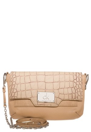 Sac bandoulière beige Calvin Klein Jeans avec rabat à texture crocodile, plaque logo argentée et bandoulière en chaîne sur fond blanc.