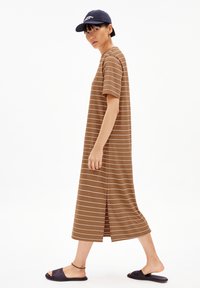 Brown striped midi dress with short sleeves, side slits, made of soft fabric. Worn with a navy cap and black slide sandals.