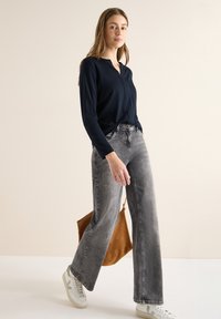 Granatowa bluzka z długim rękawem i dekoltem w serek, zestawiona z wysokim stanem jasnoszarymi szerokimi spodniami jeansowymi oraz białymi trampkami. Brązowa zamszowa torba dopełnia stylizację.