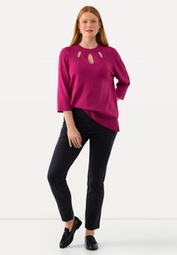 Top magenta de manga larga con cuello redondo y detalles recortados, combinado con pantalones negros ajustados y mocasines negros. Textura suave.