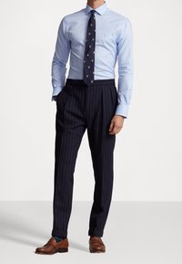 Světle modrá košile s dlouhým rukávem, tmavě modré pruhované kalhoty, vzorovaná kravata se zlatými akcenty, hnědé kožené boty, detaily z texturované látky.