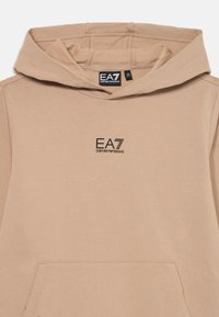 Sweat-shirt à capuche beige avec poche avant et logo noir EA7 Emporio Armani sur la poitrine et étiquette à l'intérieur du cou.