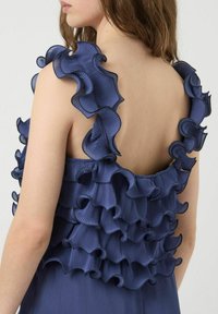 Marineblauwe top met gelaagde ruffles van textuurstof, met driedimensionale plooien langs de schouders en de rug.