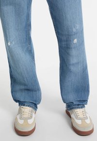 Heledad sinine kulunud teksad, lahtine lõige ja hambuline kangas. Valged ja beežid tennised hallide detailidega ning pruunide talladega, millel on paelad.