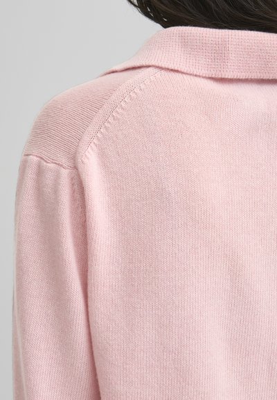 Svijetlo ružičasti pleteni pulover s rebrastim ovratnikom i šavovima na ramenima. Mekana tekstura s finim, ujednačenim detaljima šavova.