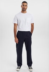 Hvid kortærmet skjorte med brystlomme, parret med marineblå elastisk taljebukser og sorte sko med hvide såler. Simpelt og funktionelt design.