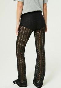 Pantaloni neri in pizzo con motivi floreali intricati e sezioni trasparenti, progettati con fondo svasato e una vita solida.