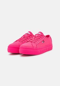 Zapatillas de lona rosas con un acabado texturizado, que presentan una suela de goma ligeramente elevada y el logo "TOMMY JEANS" en relieve en el lateral.