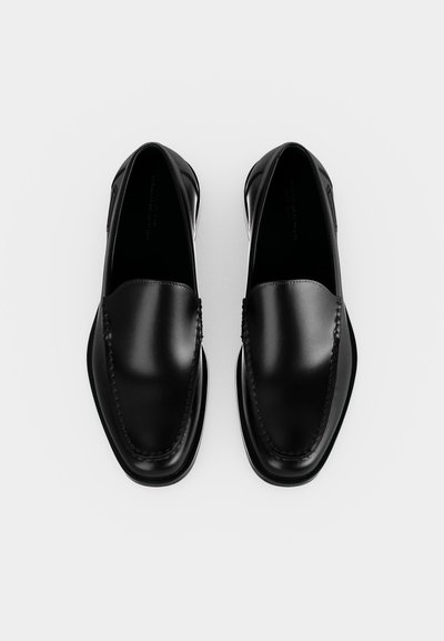 Ζευγάρι μαύρα δερμάτινα loafers με στρογγυλεμένες τετράγωνες μύτες και ορατή ραφή στο πάνω μέρος, εμφανιζόμενα από πάνω σε λευκό φόντο.