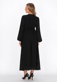 Rochie lungă neagră cu mâneci lungi, talie ajustată și fustă fluidă. Material transparent cu textură subtilă. Legată la spate. Purtați cu tocuri negre.