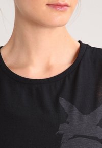 Black cotton T-shirt with a round neckline and a subtle graphic design. The fabric appears soft with a smooth texture.