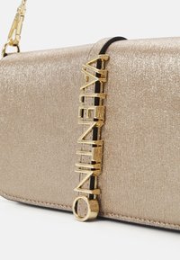 Gold glittery Valentino bag with a vertical gold logo attached to the front and a gold chain strap visible at the corner.