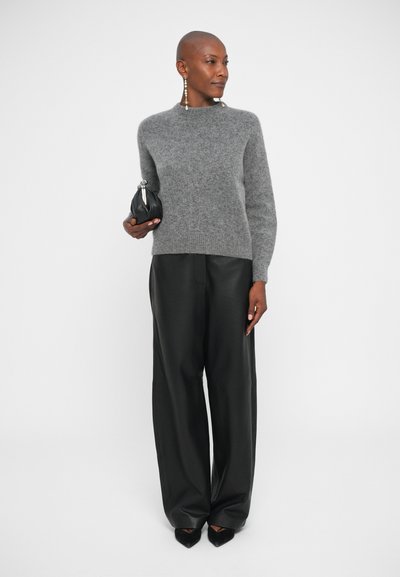 Maglione grigio e peloso con scollo a giro; abbinato a pantaloni neri in pelle a gamba larga. La modella tiene una piccola pochette nera e indossa orecchini di grande impatto.