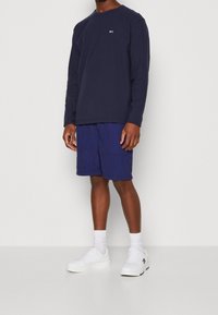 Námořnické tričko s dlouhým rukávem a logem, v kombinaci s ladícími námořnickými šortkami. Bílé tenisky a ponožky dokončují outfit. Hladká tkanina, volný střih.