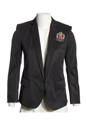 Blazer noir à fines rayures avec écusson sur la poitrine gauche et col à revers cranté sur un torse de mannequin blanc.