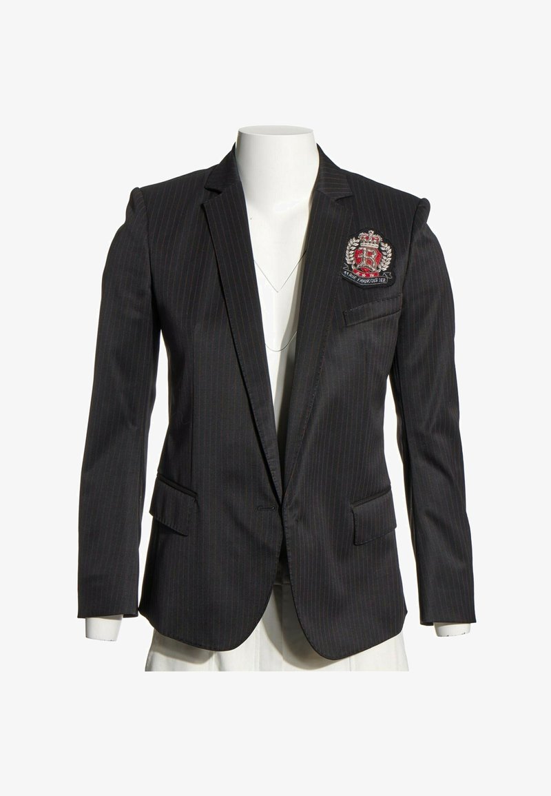 Blazer noir à fines rayures avec écusson sur la poitrine gauche et col à revers cranté sur un torse de mannequin blanc.