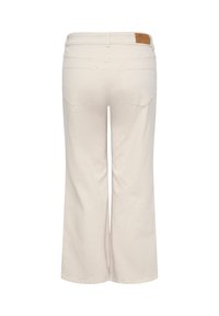 Blugi largi de culoare crem văzuți din spate, cu două buzunare în spate și o mică etichetă de brand din piele maro pe talie.