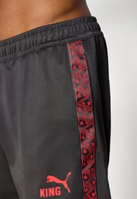 Sorte træningsshorts med elastisk waistband. Røde mønstrede sidelister og "KING" i rødt ved kanten, med Puma-logo. Glat tekstur.