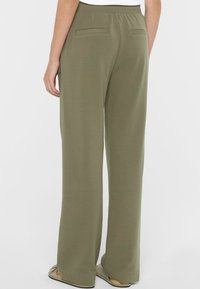 Olivgrüne, weit geschnittene Hose aus weichem Stoff, mit einem elastischen Bund und zwei Gesäßtaschen. Einfaches Design ohne sichtbare Beschläge.