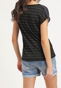 Czarny t-shirt z krótkim rękawem w białe poziome paski, z jednolitą czarną tylnią częścią i luźnym fasonem, zestawiony z dżinsowymi szortami.