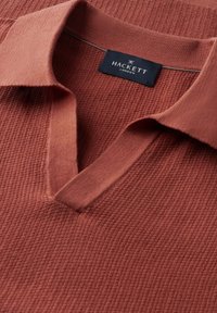 Koszulka polo w kolorze rdzy z teksturowanym dzianinowym materiałem, miękkim kołnierzem oraz metką marki "Hackett London" wewnątrz przy dekolcie.