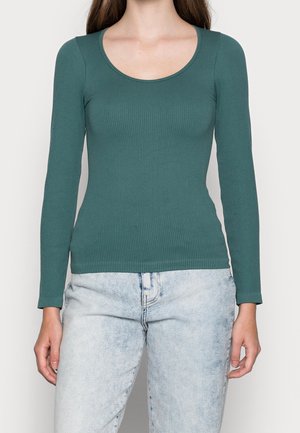 Długi rękaw, ribbed top w kolorze teal, z okrągłym dekoltem. Wykonany z miękkiej, elastycznej tkaniny, w zestawieniu z jasnoniebieskimi, wyblakłymi dżinsami.