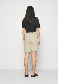 Shorts beige con taglio dritto, orlo risvolto e due tasche posteriori, abbinati a una t-shirt nera e scarpe slip-on nere.