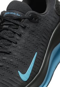Čierna športová obuv s textúrovaným pleteným zvrškom, na bočnej strane so svetlomodrým logom Nike a s odpruženou, zakrivenou čiernou podrážkou.