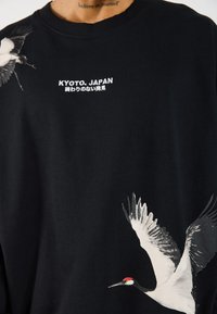 Black cotton t-shirt featuring white cranes, "KYOTO, JAPAN" text, and fine detail on wings, creating visual contrast and interest.
