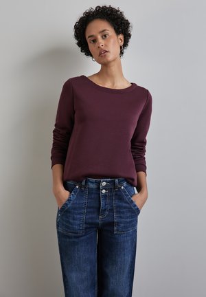 Bordeauxkleurig langemouwtop met een ronde hals, gecombineerd met hoog-was gevoerde, wijde blauwe jeans met zakaccenten en een vervaagde was.