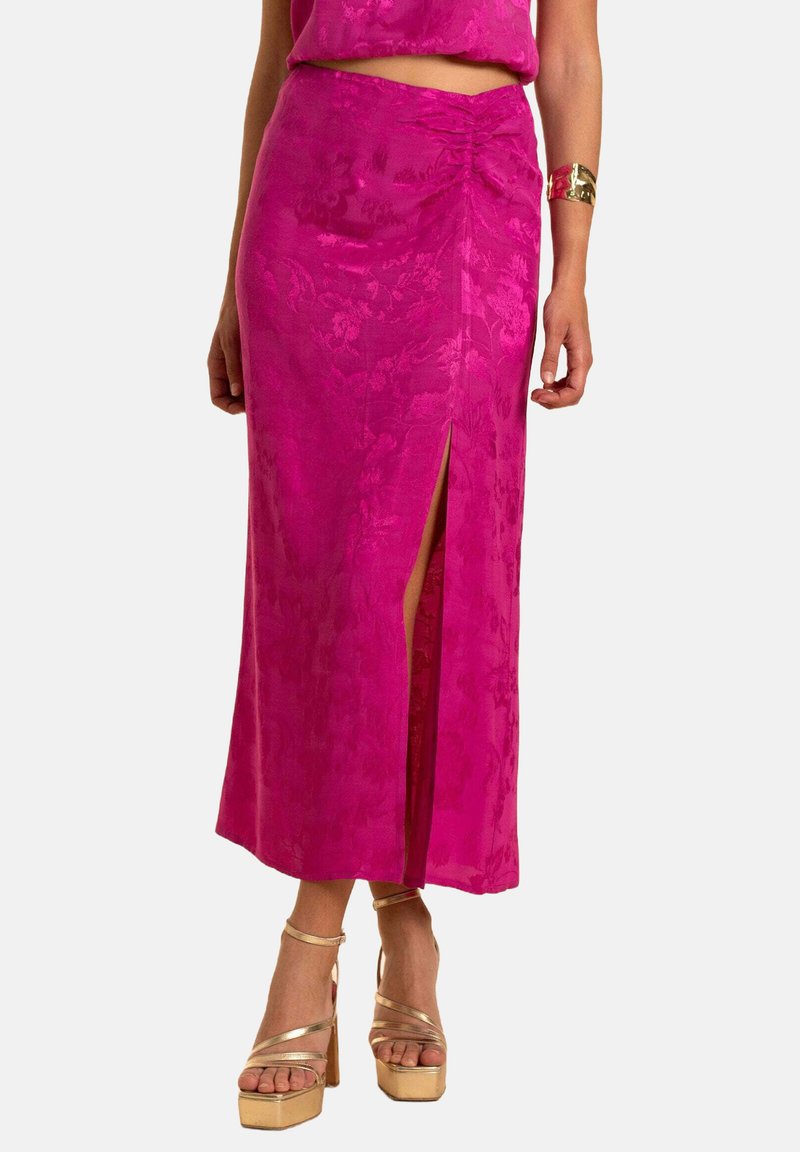 Jupe fuchsia avec une fente latérale, ornée d'une texture florale. Assortie avec des sandales à plateforme dorées et un top coordonné.