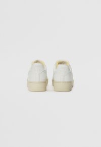 Un par de zapatillas Nike Air blancas vistas desde atrás, con suelas beige y sutil grabado del logo de Nike Air en la pestaña del talón.