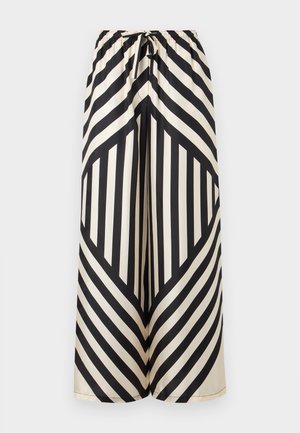 Woman wearing black and white geometric striped wide-leg pants and matching loose top, standing with hands in pockets against a plain background.