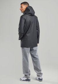 Black waterproof coat with a hood, long sleeves, and a smooth texture, paired with light gray pants and white sneakers.
