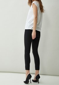 Haut blanc à manches courtes associé à un pantalon noir ajusté et des talons hauts noirs, mettant en avant un design simple et épuré.