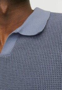 Pletená polo košile v světle modré barvě, se strukturovaným tkaním, plochým límcem a designem ve tvaru V, zaměřující se na neformální styl.