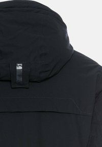 Schwarze Kapuzenjacke mit glatter Textur, sichtbaren Nähten und einem glänzenden Akzent am Riemen der Kapuze, kombiniert mit einem modernen Design.