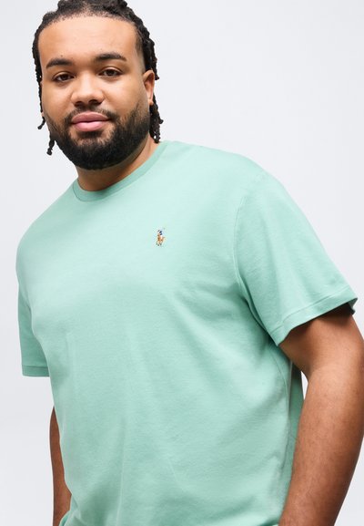 Άνδρας με κοντά dreadlocks και γένια, που φοράει ανοιχτοπράσινο μπλουζάκι με μικρό κεντητό λογότυπο παίκτη πόλο στο στήθος.