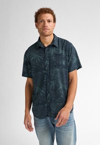 Camisa de manga corta abotonada en azul oscuro con un patrón de hojas verdes, presenta un bolsillo en el pecho, tela suave y un corte relajado.