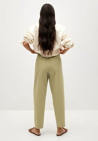 Chemise oversize beige clair à manches retroussées, associée à un pantalon taille haute vert olive et des tongs marron, vue de dos.