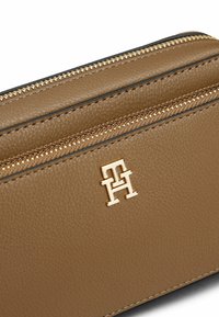 Cartera de cuero texturizado marrón con herrajes en tono dorado, que cuenta con varios compartimentos con cremallera y un acento de logo en la parte delantera.