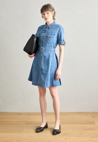 Denim krekliņš ar īsām piedurknēm, pogu aizdare, divas krūšu kabatas un josta viduklī. Saskaņots ar melnu somu un plakanām kurpēm.