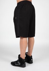 Black athletic shorts with an elastic waistband, textured fabric, and side zip pockets, paired with black high-top sneakers.