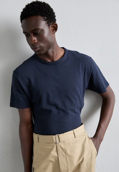 T-shirt en coton bleu marine avec un col rond, des manches courtes et une coupe décontractée, associé à un pantalon beige avec une ceinture à clip.