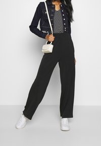 Veste en denim courte avec fermeture à boutons, pantalon large noir, top rayé et petit sac bandoulière blanc. Des baskets blanches complètent l'ensemble.