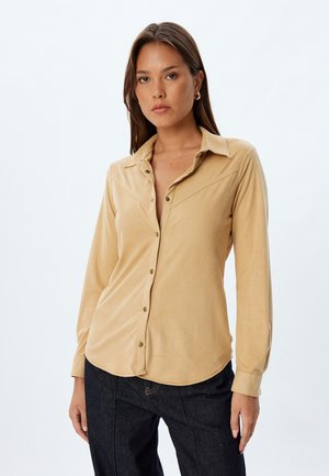 Beige knoopshirt gemaakt van zachte stof, met een kraag, lange mouwen en een afgeronde zoom met zichtbare knoopdetails.