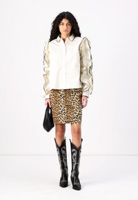 Vit skjorta med volangärmar, mini kjol i leopardskrift och svarta cowboyboots med vit brodering. Modellen håller en svart väska.