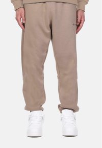 Pantalons de survêtement beige à coupe décontractée, avec des poches latérales et des poignets élastiques, associés à des baskets montantes blanches.