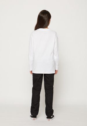 White long-sleeve shirt with a round neck and relaxed fit, paired with black pants and black sneakers, viewed from the back.